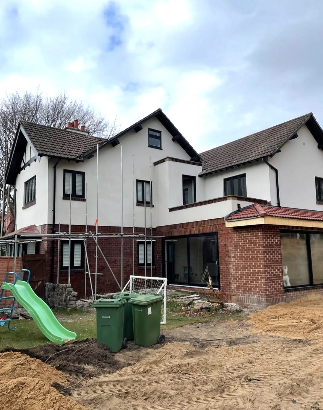 Back of a house half rendered with scaffold over a brick extension