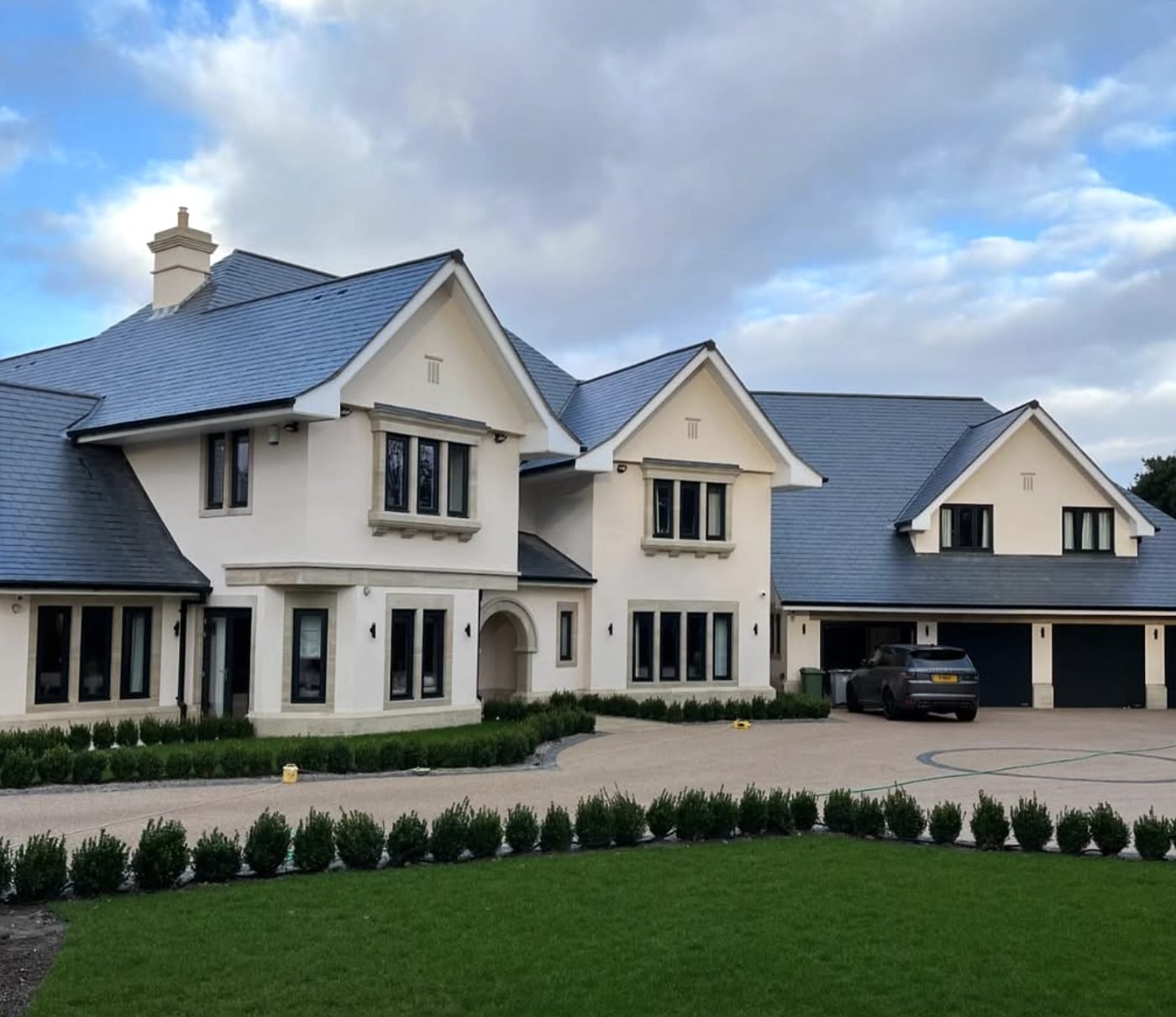 Large detached house finished in cream render with a lawn and gravel drive