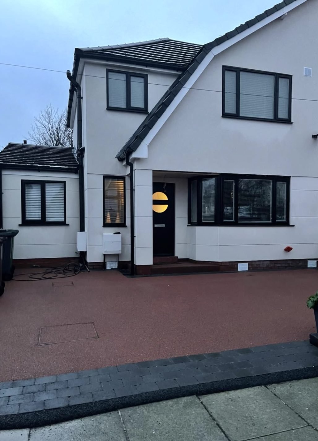 House in white render with dark window frames and a red paved drive